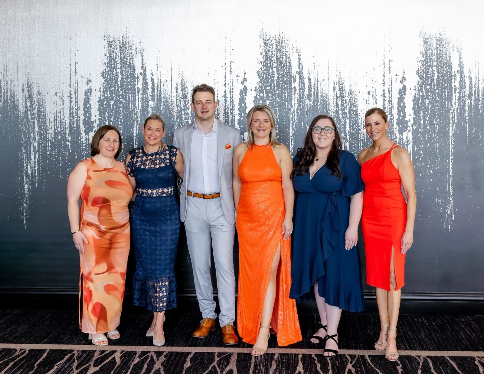 Six guests in bright gowns and a suit at a Brilora gala